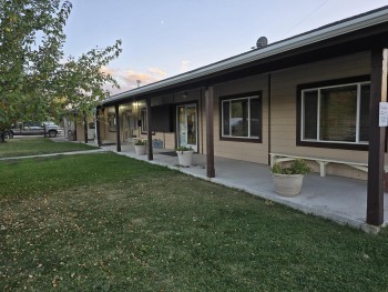 A one-story building with three windows, a door, and five posts and a patio.