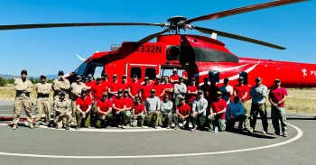 A crew of firefighters poses in front of a firefighting helicopter.