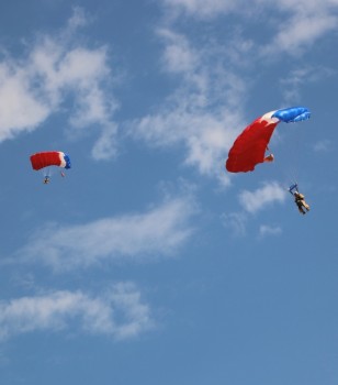 Two smokejumpers with red-and-white parachutes in the air