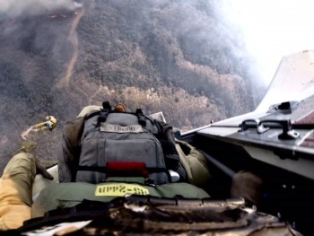 Person wearing parachute exits plane with burnt forest below