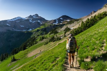 A hiker walks along the trail on a ridgeline toward snow-spotted mountains.