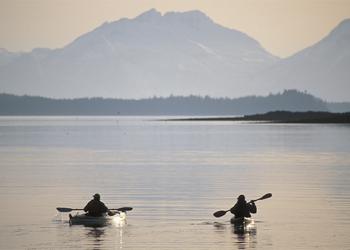 Two kayakers are silhouetted in sunset view.