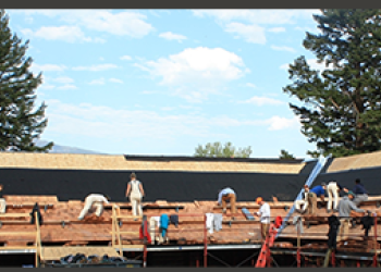 A photo of about 16 people working on a wide roof of a lodge.