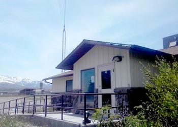 Angle view of the front of the Mountain City-Ruby Mountains-Jarbidge Ranger District's Wells Office that is cream with dark brown trim and roof and a long sloping sidewalk and brown railings.