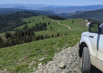 A Forest Service truck is parked high on a mountain top with a dirt road in the background.
