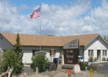 An American flag flies in the blue sky above the office building and the sign out front. 