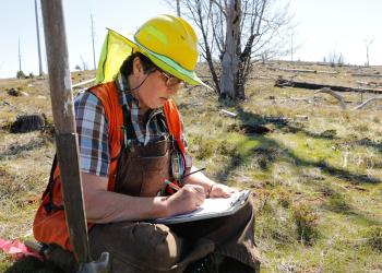 A woman writes notes on a clipboard outside.