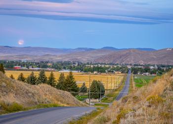 A rural highway with a town and mountains in the background.