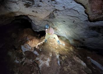 A photo of a person sitting inside a cave with a headlamp.