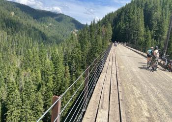 Two cyclists rest and enjoy the scenery on a large wooden trestle at the Route of the Hiawatha