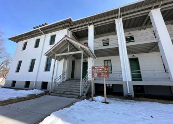 A white two story building with covered walkway and balcony. A sign in front reads: Regional Headquarters, Northern Region. Forest Service.