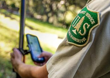 A Forest Service worker in a uniform looks at the screen of a data collection field computer.