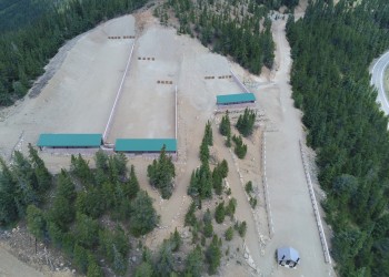 Aerial view of three shooting galleries and the green shade structures against a forested landscape.
