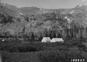 A historical photograph of two tents in a high mountain meadow