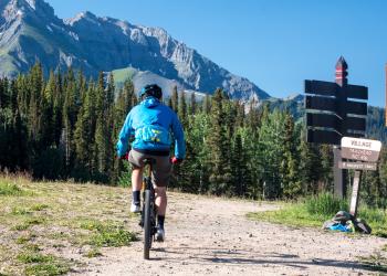 A person wearing a blue jacket and helmet rides a mountain bike on a dirt mountain trail