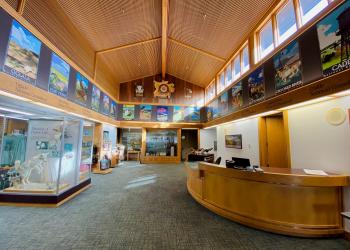 Interior view of the National Grasslands Visitor Center lobby. The walls are white and brown with colorful posters and exhibits throughout the room. 