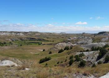 A picturesque valley surrounded by flat topped buttes with bright blue sky and white clouds.