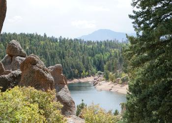View of reservoir from above between boulders and trees with forest and mountain in the background.