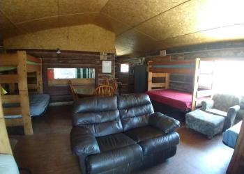 Interior living room of a log cabin with bunk beds and a leather couch and other living room furniture.
