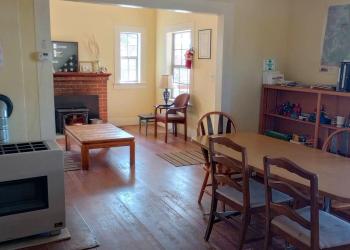 Open dining room and living room with a propane heater, fireplace, kitchen table and chairs, coffee table, bookshelves,  and a couch.