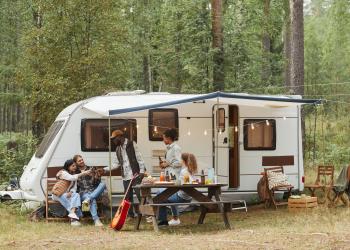 Several people sit outside of a camper with a canopy and lights around the top of it.