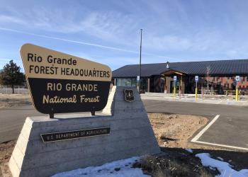 A brown and yellow sign signifies the Rio Grande National Forest headquarters from across the parking lot. 