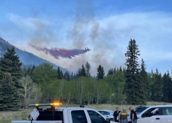 An air tanker is seen through light smoke dropping red fire retardant.