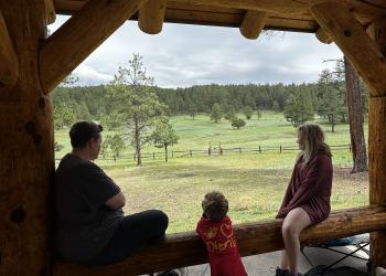 People lean on a railing and look out over a meadow.