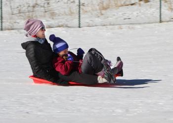 An adult and a child share a sled in the snow