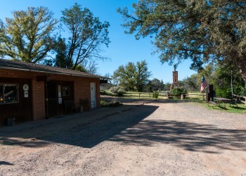 A brick building sits to the left side of the photo while a dirt lot and a picnic table sit to the right