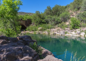 A blue-green body of water is visible between rocks and green trees