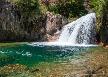 A waterfall flows off of rocky cliffs into a blue-green body of water