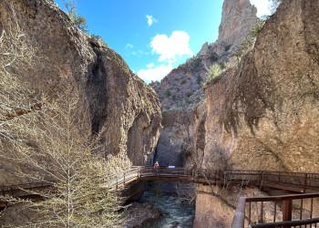 People stand on a pedestrian bridge suspended above a rushing creek