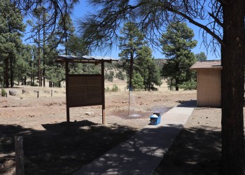 Photo of a sidewalk beside an interpretive sign, leading to a restroom.
