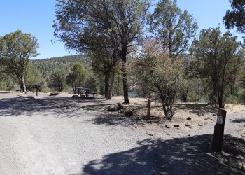Photo of a campsite with site marker, picnic table, fire ring, and grill under a mix of sun and shade