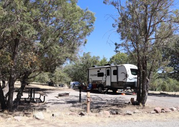 Photo of a campsite with site marker, picnic table, fire ring, and grill under a mix of sun and shade