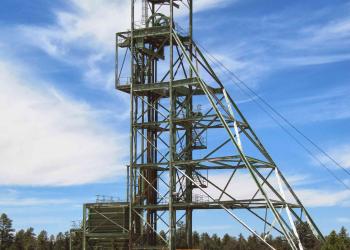 A metal mining structure rises above bare ground with trees in the background.