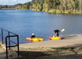 Two people putting kayaks in the lake at a boat ramp.