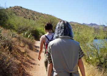 Two girls are pictured hiking on Butcher Jones Trailhead with Saguaro Lake and a desert landscape in the background