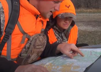 Two hunters dressed in camouflage and bright orange point toward a map.