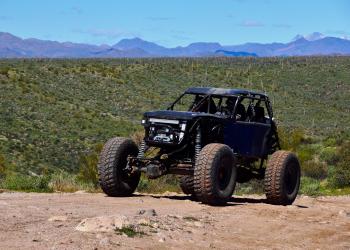 A blue off highway vehicle is seen driving in a Tonto OHV Permit Zone with a beautiful mountain landscape in the background.