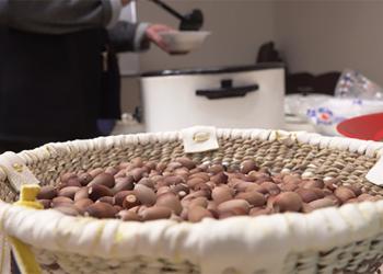 A bowl of harvested Emory Oak acorns in the foreground and in the background a person dishes out acorn soup from a crockpot.
