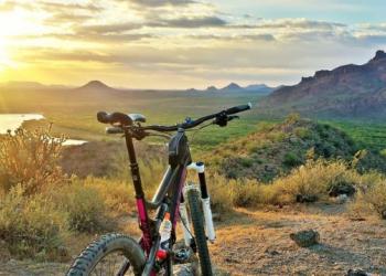 A red mountain bike is pictured while the sun is spotted atop mountains