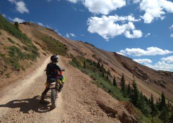 A person on a motorcycle takes a break on a dirt road.