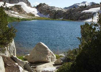 A lake surrounded by mountains, trees and a little snow