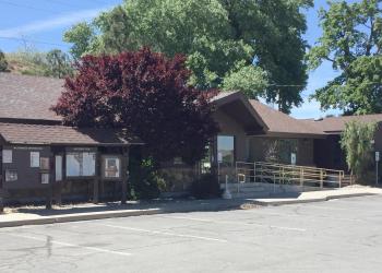 A side view of the dark brown Carson Ranger District office with a wheelchair-accessible ramp, surrounded by trees and a bulletin board displaying information.