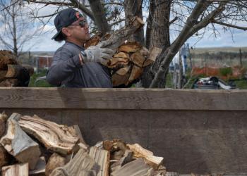 With gloved hands, Tribal members unload split firewood from inside the back of a trailer. 