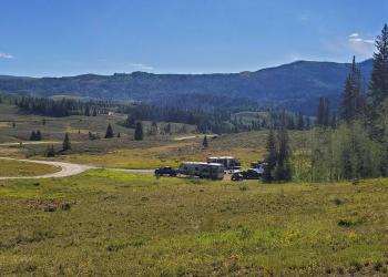 a scenic landscape with a road and a couple of cars with mountains in the background