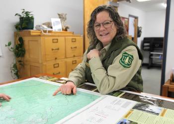 A woman in a Forest Service uniform points at a visitor map.