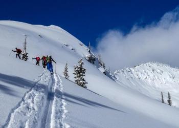 A group of backcountry skiiers skins up a snowy mountainside.